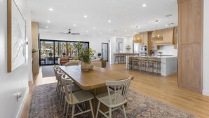 Une cuisine moderne avec des meubles en bois, un coin repas doté d’une grande table et de chaises, et une vue sur l’extérieur grâce à des portes vitrées.