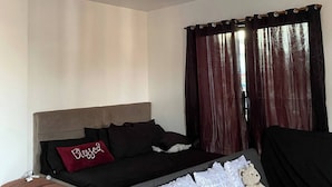 A modern bedroom with a bed, a sofa, a teddy bear, and a window with curtains.
