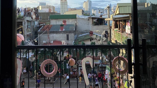 A view from a balcony with a metal railing, overlooking a playground with children playing and a cityscape in the background.