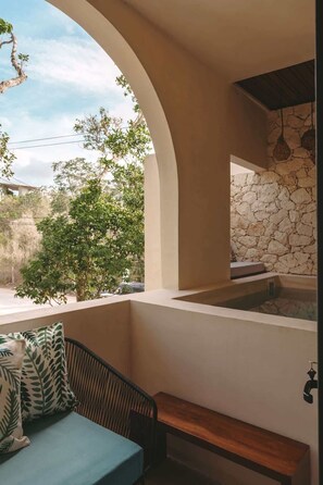 A room with a stone wall, a bench, and a view of trees and a building outside.