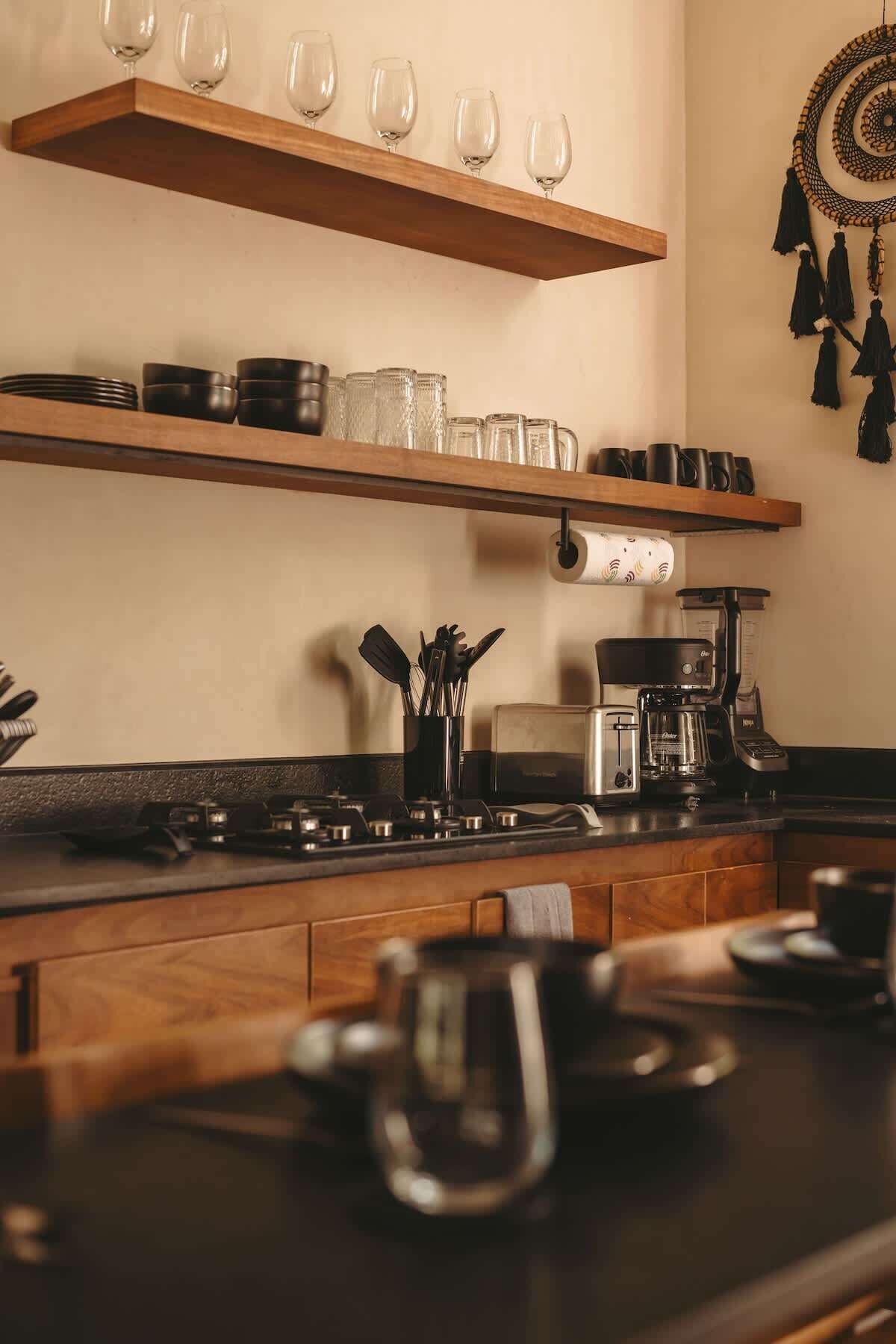 Una cocina con estantes de madera que sostienen cristalería y utensilios de cocina, una cafetera y un tostador.