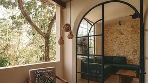 A room with a view of trees through a large window, a green sofa, and a wooden chair with a patterned pillow. - Boutique La Veleta Condo with Private Pool Terrace (Tulum)