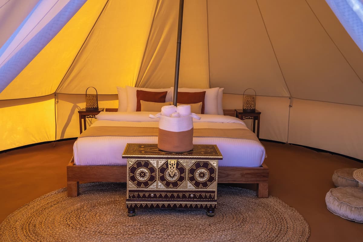 A tented room with a bed, pillows, a bedside table with a lamp, and a decorative chest.