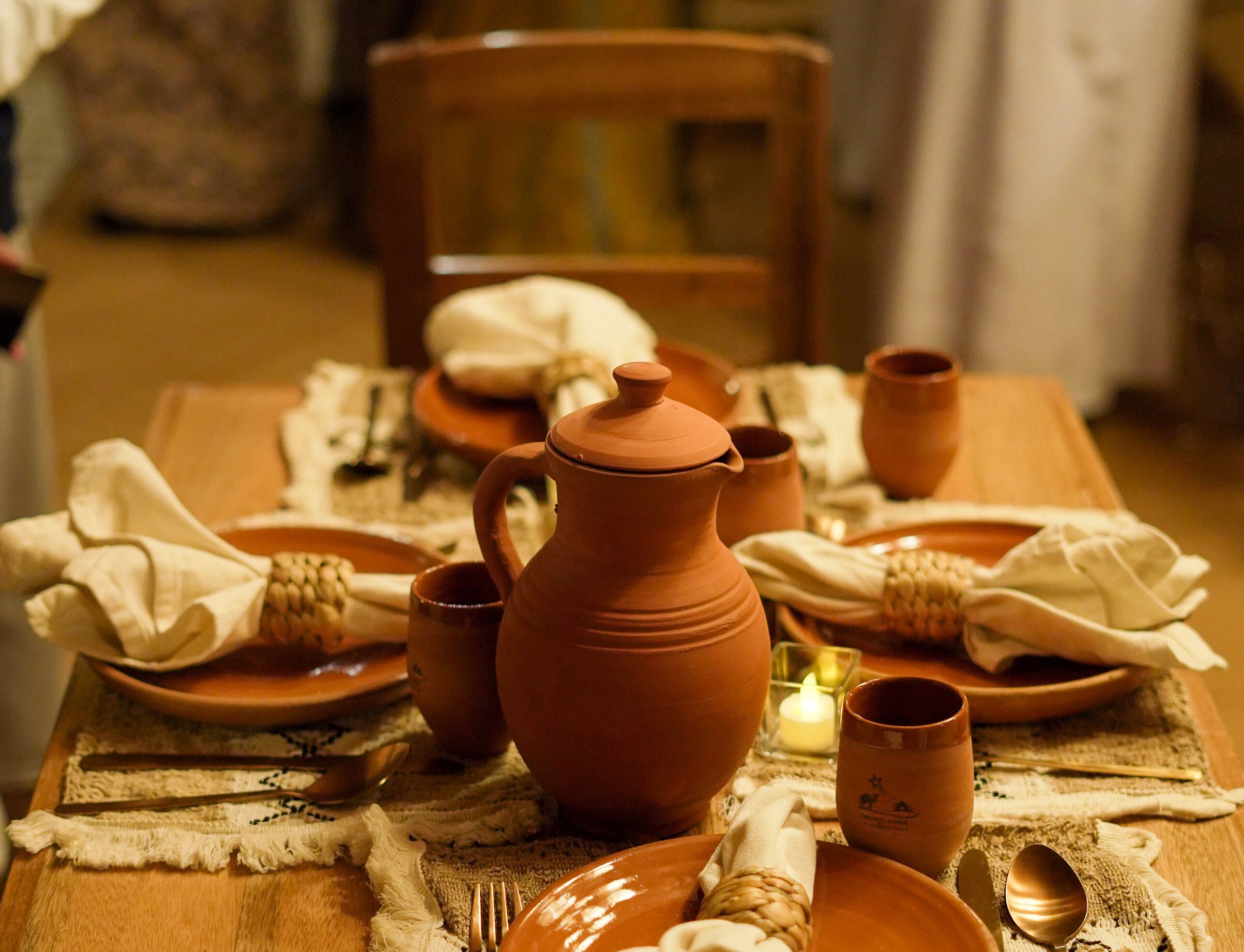 Une table à manger dressée avec de la vaisselle en terre cuite, comprenant un pichet, des tasses et des assiettes, disposés sur un set de table en fibres tressées.