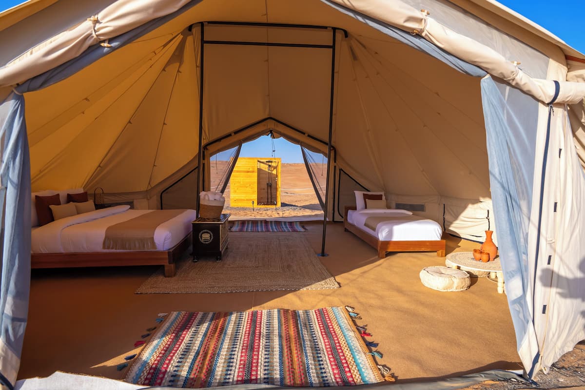 A tent with two beds, a small table, and a view of the desert.