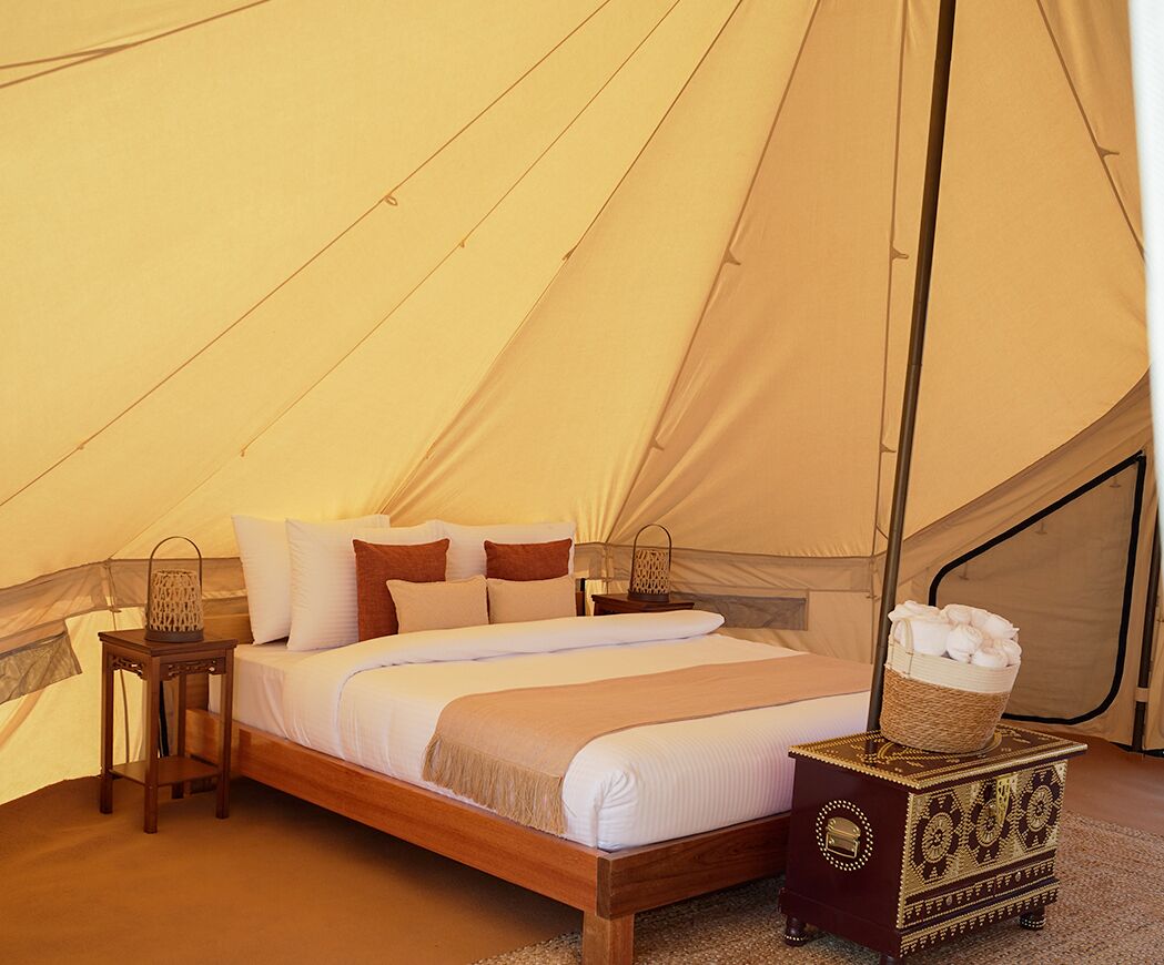 A tent with a bed, pillows, a bedside table with a lantern, and a decorative chest.