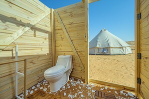 Interior de madera con un inodoro y vista a una carpa en el exterior.