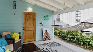 Un porche abrité avec une porte en bois, un hamac et une décoration murale représentant des poissons.
