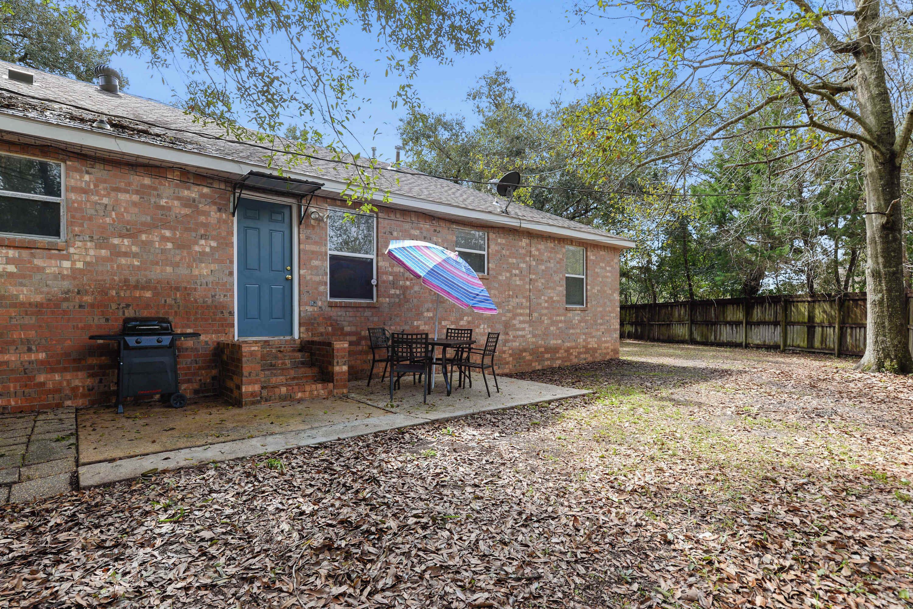 A brick house with a blue door, a barbecue grill, and a patio with chairs.
