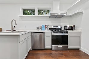 A modern kitchen with a dishwasher, oven, microwave, and a window above the sink.