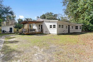 A single-story white building with a covered porch, a small adjacent shed, and a grassy yard.