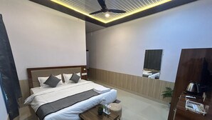 Una camera d'albergo moderna con un letto grande, un comodino in legno, un piccolo tavolino con una pianta in vaso e uno specchio a parete.