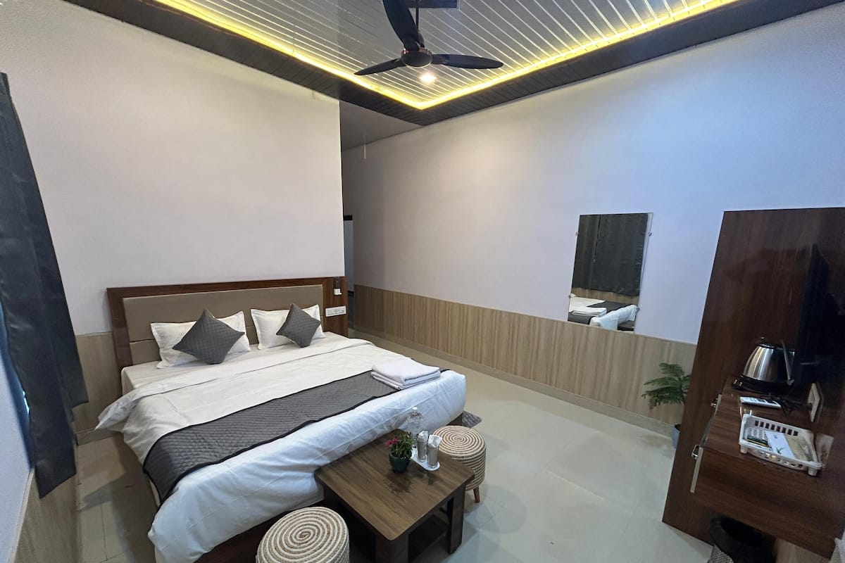 A modern hotel room with a large bed, a wooden nightstand, a small table with a potted plant, and a mirror on the wall.