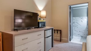 A compact hotel room with a flat-screen TV, a small refrigerator, a microwave, and a bedside table.