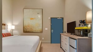 A hotel room with a bed, a desk with a television, a coffee maker, and a door.
