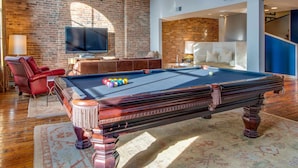 A pool table in a room with a brick wall, a television, and a leather chair.