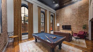 A billiards table in a room with brick walls, large windows, and a cozy seating area.