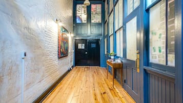 Un couloir doté d’un plancher en bois, d’un mur en briques blanches et d’une porte bleue avec des panneaux de verre.