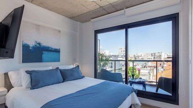 Una habitación de hotel moderna con una cama grande, televisión de pantalla plana, balcón con vistas a la ciudad y un cuadro en la pared.