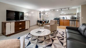 A modern living room with a flat-screen TV, a coffee table, and a sofa. There is a kitchen area with a microwave, oven, and refrigerator. - Charming Stay for 4 in DT, Walk to Broadway! (Nashville)