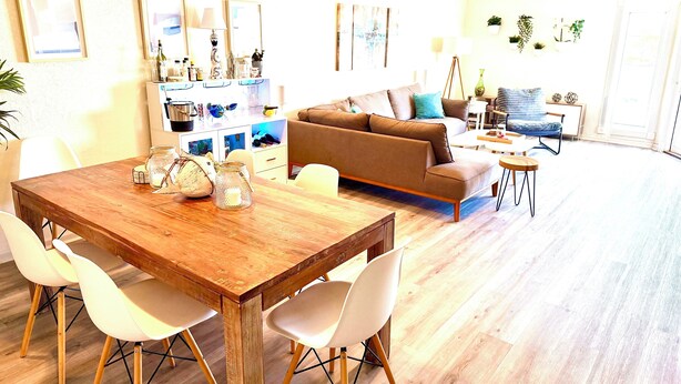 A spacious living area with a wooden dining table, white chairs, a brown sofa, and a coffee table.