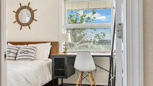 A bedroom with a bed, a desk, a chair, a window with blinds, and a mirror on the wall.