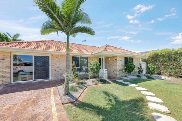 A two-story house with a tiled roof, a brick exterior, and a well-maintained lawn with stepping stones leading to the front door. - Urban Getaway Bargara Central (Bargara)