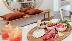 Un comedor con un espejo redondo, una mesa de madera con una bandeja de fruta y queso, y dos vasos de una bebida roja.