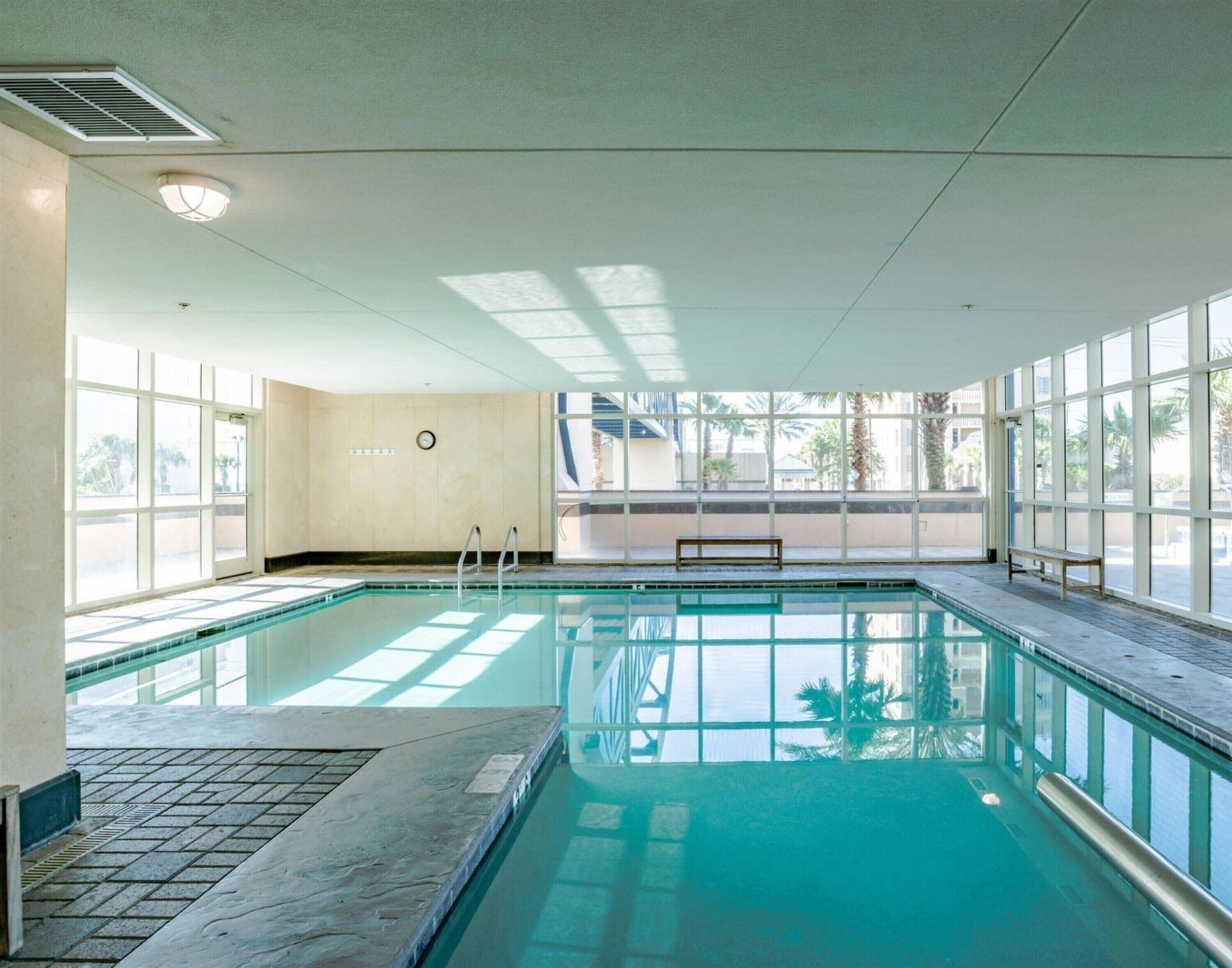 An indoor swimming pool with clear glass walls, a bench, and a clock on the wall.