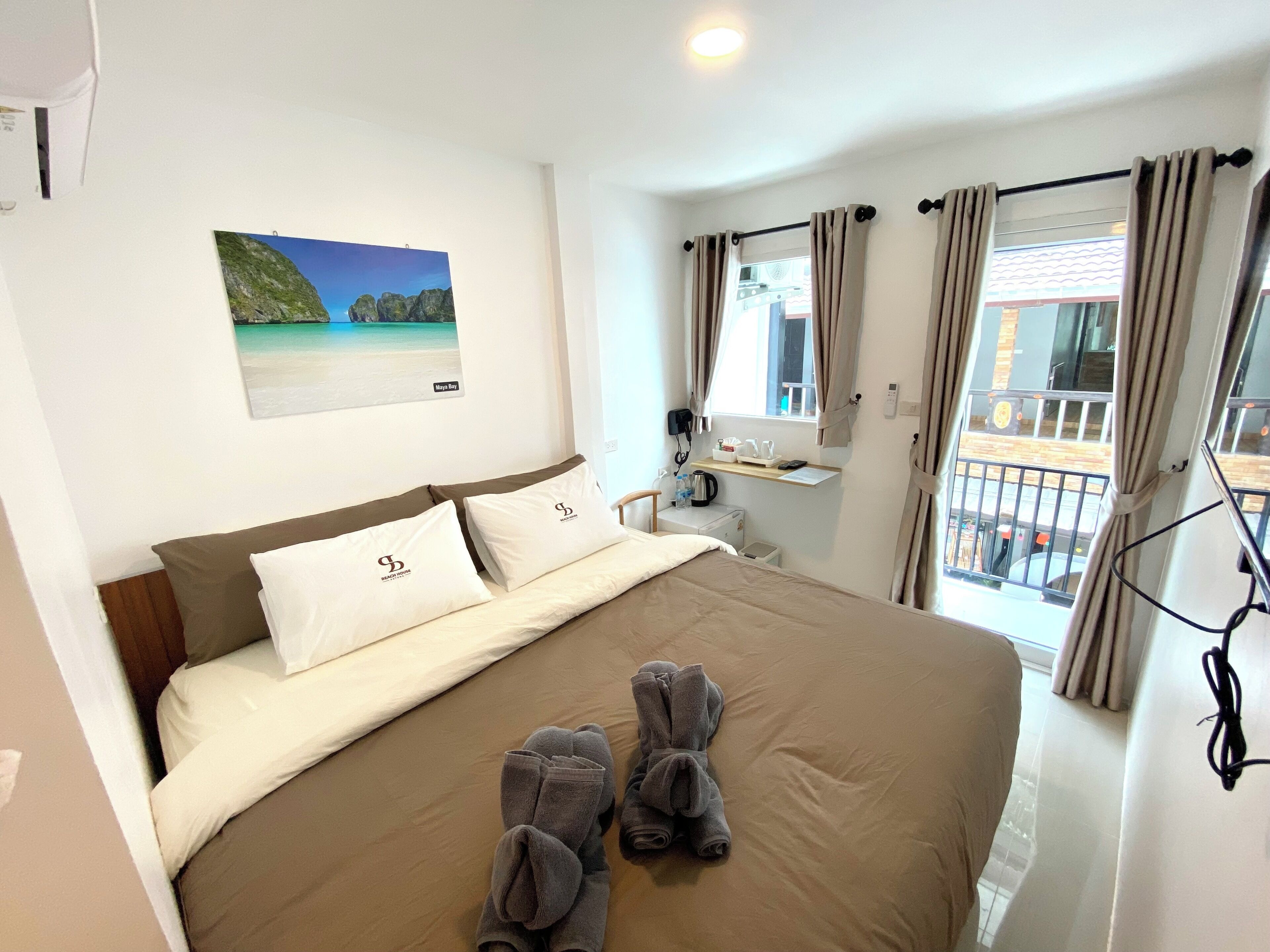 A hotel room with a bed, a desk with a computer, a window with curtains, and a painting on the wall.