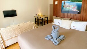 A hotel room with a large bed, a flat-screen TV mounted on the wall, a wooden panel wall, and a painting of a coastal scene. - SJ Beach House Patong (Patong)