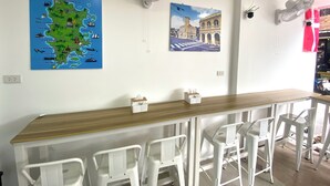 A room with a wooden table, white chairs, a map of Phuket, and a cityscape picture. - SJ Beach House Patong (Patong)