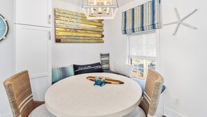 A round table with a surfboard and decorative items, surrounded by wicker chairs, in a room with a nautical theme including a starfish wall decoration and a striped window valance.