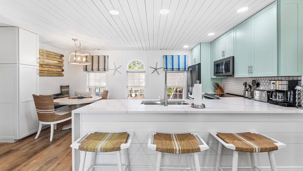 A modern kitchen with white cabinetry, a central island with bar stools, and a wooden ceiling.
