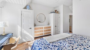 A bedroom with a bed, a dresser, a desk, and a mirror.