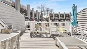 A deck with outdoor seating, a white fence, and a view of adjacent buildings.