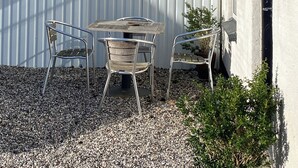 Un patio con una mesa y dos sillas, un cerco blanco y un edificio con una puerta y una ventana.