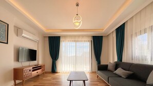 A modern living room with a flat-screen TV, a wooden cabinet, a grey sofa, and a coffee table.