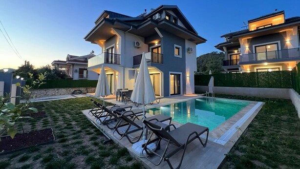 A two-story house with a swimming pool, outdoor seating, and a well-maintained lawn.