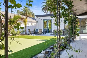 Une terrasse extérieure moderne, dotée d’une pelouse, d’un espace salon et d’une porte vitrée donnant accès à un bâtiment.