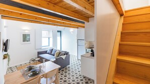 A modern kitchen with wooden beams, a dining area with a table set for two, and a living area with a sofa and a coffee table. - A Window to Porto - Pestana Lovely House (Porto)