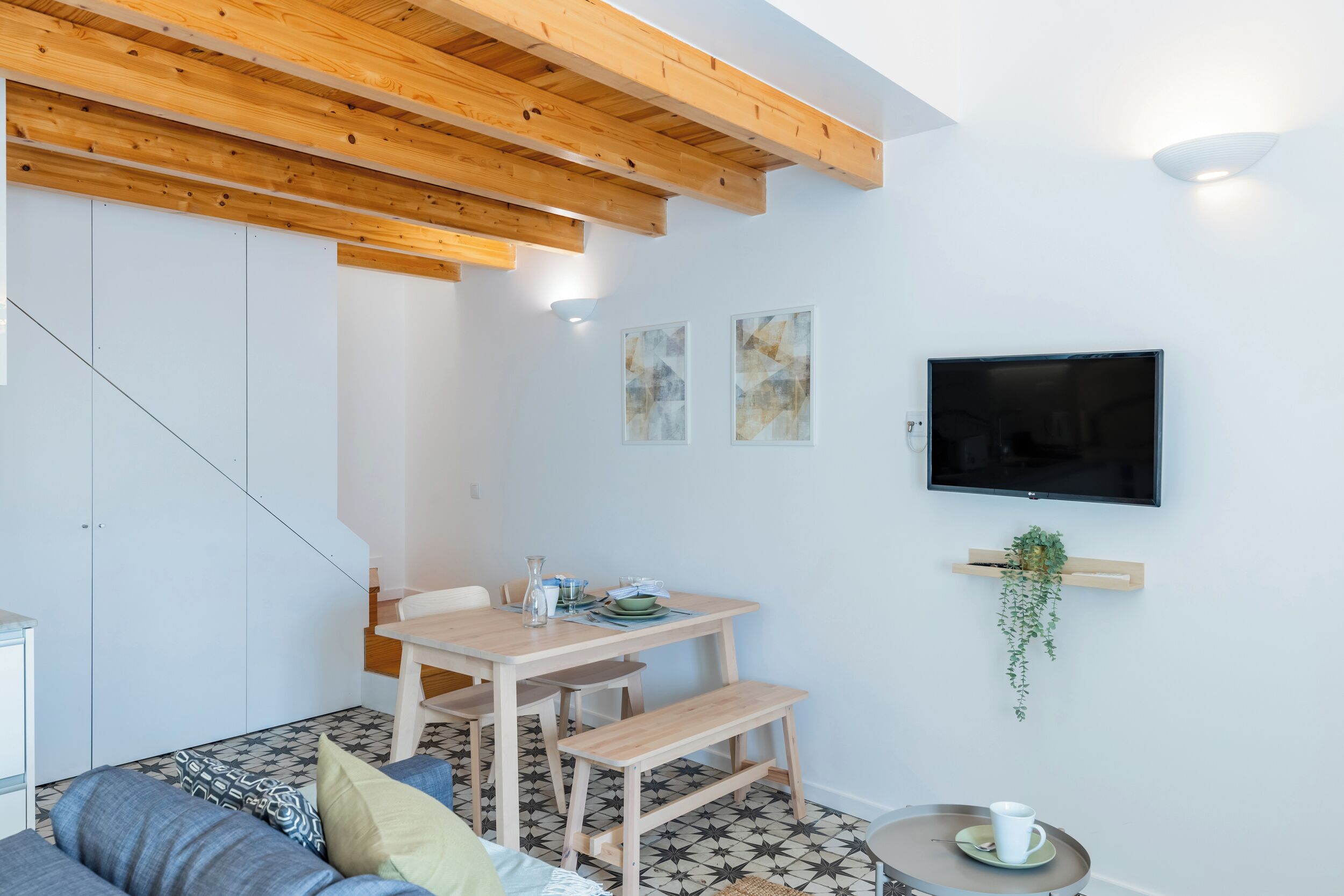 Una sala de estar moderna con techo de madera, comedor, sofá, televisor y una pequeña mesa con una taza.