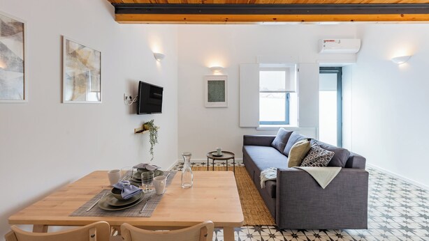 A modern living room with a wooden ceiling, a grey sofa, a dining table set with plates and glasses, and a TV mounted on the wall. - A Window to Porto - Pestana Lovely House (Porto)