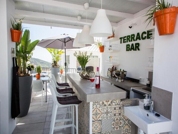 A terrace bar with a tiled backsplash, white bar stools, hanging pendant lights, and potted plants. - Almijara Residence (Cómpeta)