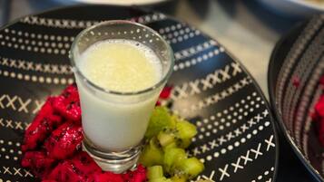 Una mesa con platos de comida, incluyendo un vaso de una bebida cremosa y frutas cortadas.