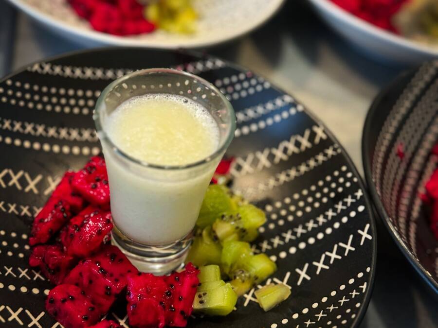 Una mesa con platos de comida, incluyendo un vaso de una bebida cremosa y frutas cortadas.