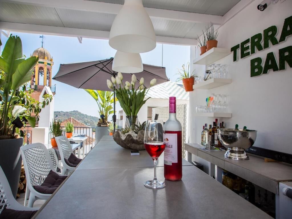 Zona de bar con vistas a una torre campanario, plantas en macetas y una botella de vino tinto sobre la barra.