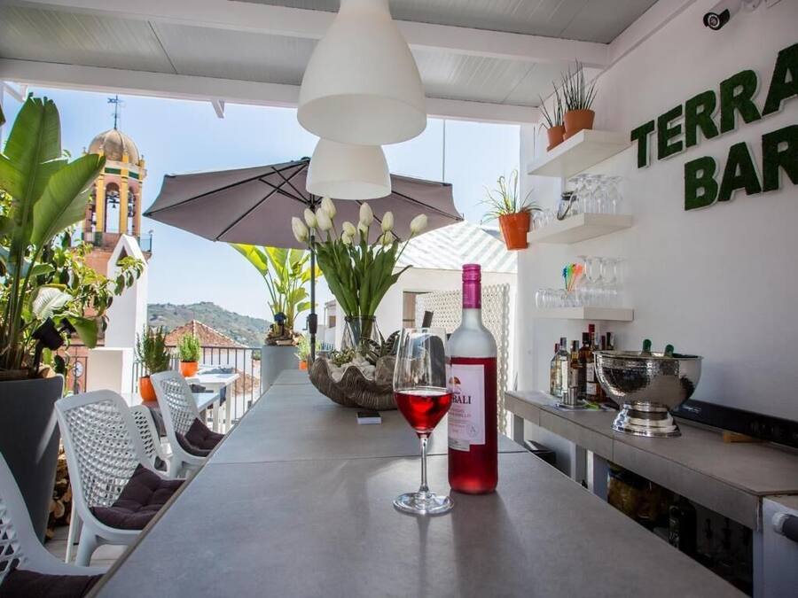Zona de bar con vistas a una torre campanario, plantas en macetas y una botella de vino tinto sobre la barra.