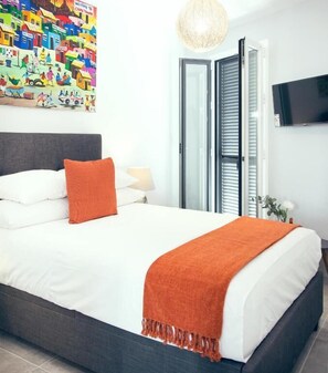 A bedroom with a bed, pillows, a blanket, a wall art, a TV, and a window with blinds. - Almijara Residence (Cómpeta)