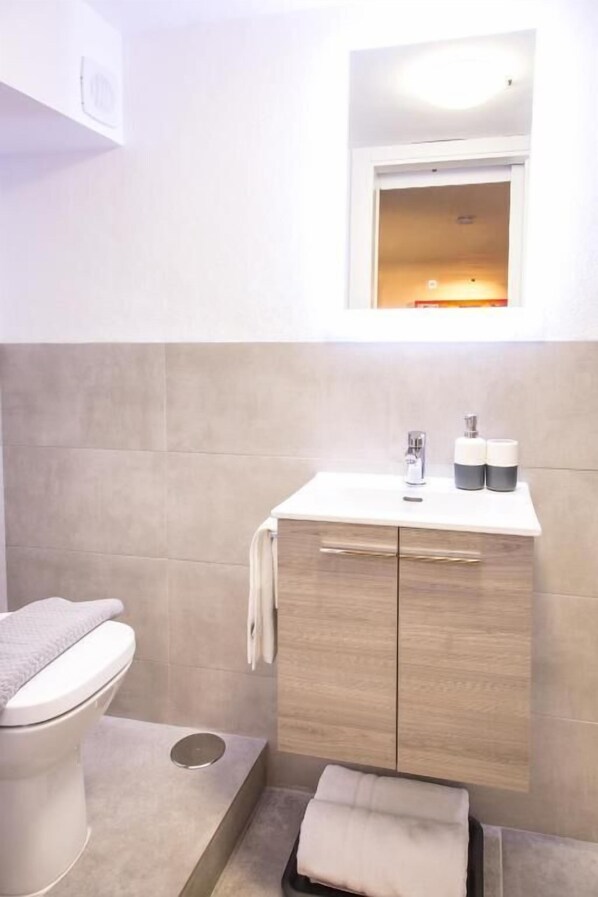 Une salle de bain moderne équipée de toilettes, d’un lavabo avec un miroir au-dessus et d’un porte-serviettes.
